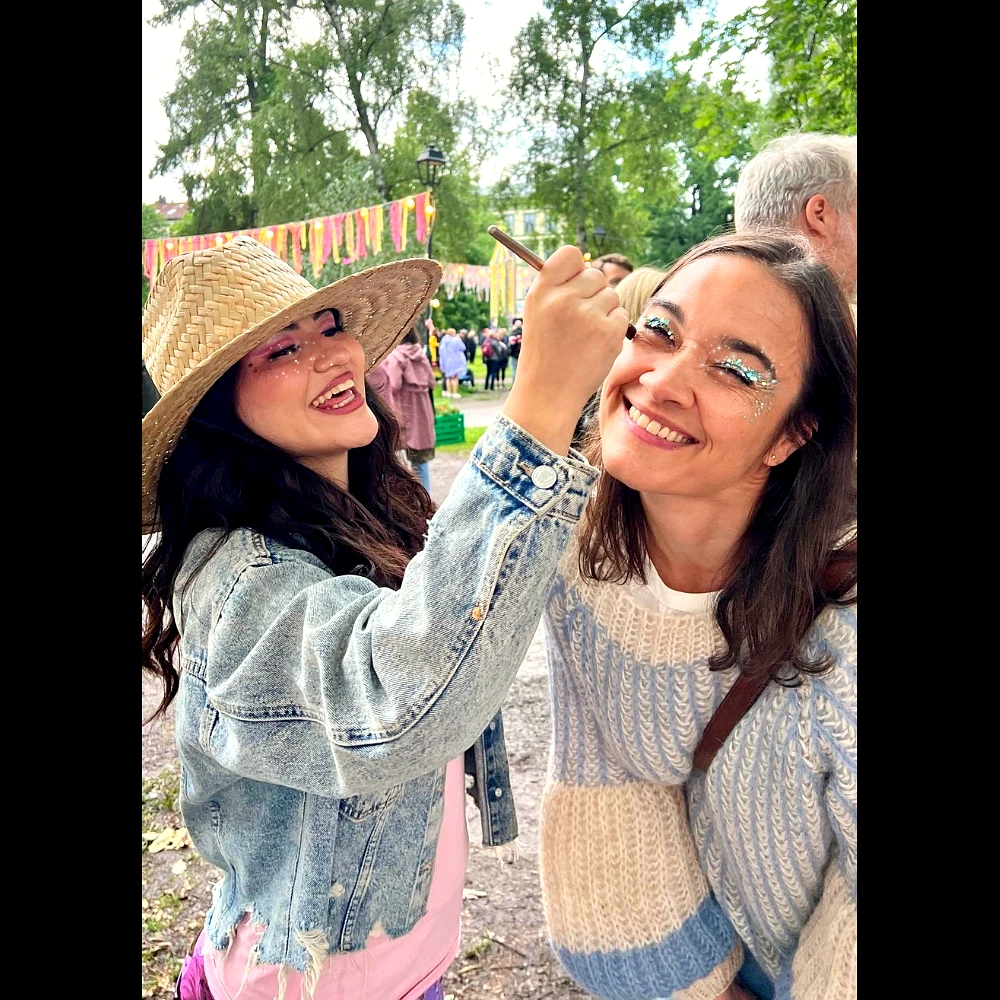 Applying plant-based Glitter Eco Lovers glitter to a smiling friend's eyes at an outdoor festival